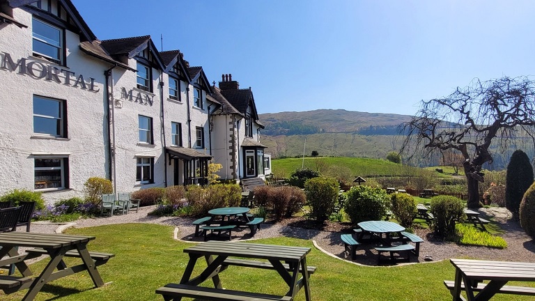 The outside of the dog-friendly Mortal Man, a dog-friendly pub in the Lake District with a lovely sun-kissed garden and far-reaching views. Benches and picnic tables are outside.